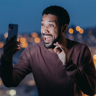 A cheerful young man taking selfie on balcony with urban view.