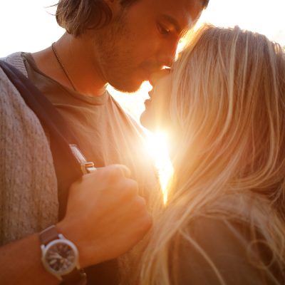 Happy smiling couple in love hug and kiss each other in the amusement park. Sunny warm spring evening